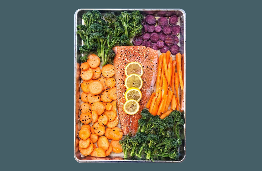 Salmon with lemon next to mixed vegetables on a sheet tray